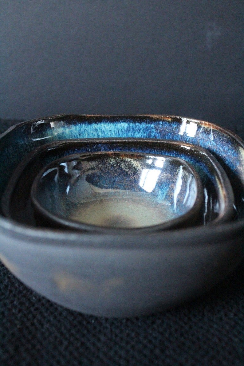 Puede incluir: Un juego de tres cuencos encajables con un esmalte azul oscuro y negro. Los cuencos est&aacute;n hechos de cer&aacute;mica y tienen una forma ligeramente irregular.