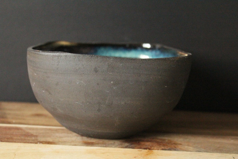 Puede incluir: Un cuenco de cer&aacute;mica gris oscuro con un esmalte azul y verde en el interior.