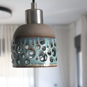 May include: A light blue ceramic pendant light fitting with a silver metal top and a pattern of small holes. The light fitting is hanging from a ceiling.