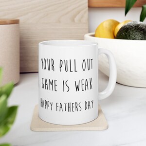 Puede incluir: Taza de café de cerámica blanca con texto negro que dice "Your pull out game is weak Happy Fathers Day".