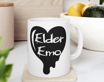 May include: White ceramic mug with a black dripping heart design. The heart has the words "Elder Emo" written in white inside.