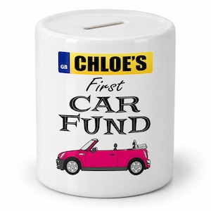 May include: A white ceramic money box featuring a yellow British license plate graphic with the text CHLOE'S, followed by the words First CAR FUND in black lettering, and a pink convertible car illustration at the bottom with a coin slot on top.