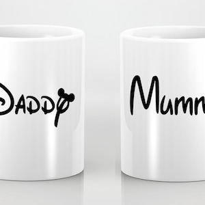 Könnte beinhalten: Zwei weiße Keramikbecher mit schwarzem Text. Ein Becher sagt "Daddy" mit einem Mickey-Mouse-Ohren-Design. Der andere Becher sagt "Mummy" mit einem Minnie-Mouse-Ohren-Design.