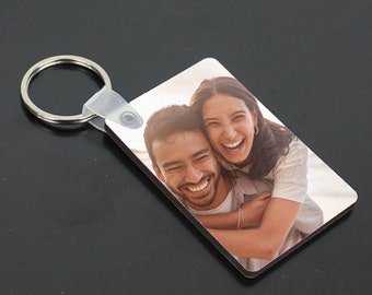Puede incluir: Un llavero de foto con una pareja sonriendo y abrazándose. El hombre lleva una camisa blanca y la mujer lleva una camisa blanca. El llavero está unido a un llavero plateado.
