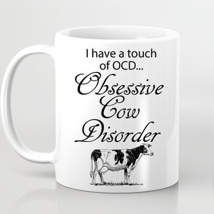 May include: White ceramic mug with a black and white illustration of a cow and the text "I have a touch of OCD... Obsessive Cow Disorder".