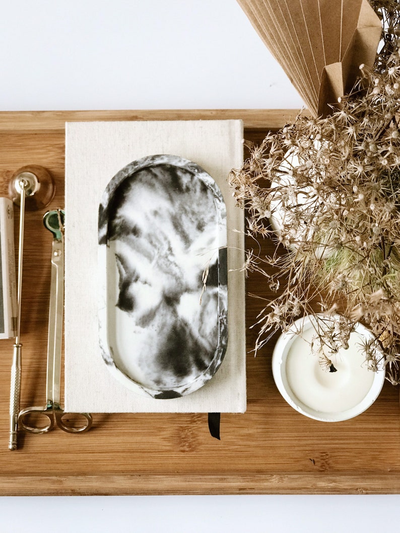 Pu&ograve; includere: Un vassoio decorativo con un motivo marmorizzato bianco e nero &egrave; appoggiato su un vassoio di legno, accanto a una candela, un taccuino e accessori per candele color oro. Fiori secchi e un ventaglio di carta completano la composizione. Il vassoio &egrave; lungo circa 15 cm.