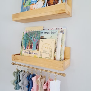 May include: Two wooden shelves with a gold metal rod underneath. The shelves are filled with children's books. The rod has several colorful fabric headbands hanging from it.