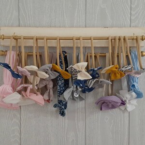 May include: A wooden headband organizer with a cream-colored base and gold accents. Various headbands and bows in shades of pink, blue, gray, and yellow are displayed on the organizer, showcasing a variety of patterns and textures.
