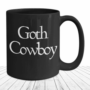 May include: Black ceramic coffee mug with white text that reads "Goth Cowboy".
