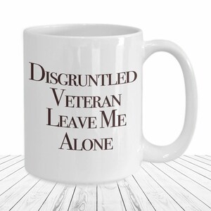 May include: White ceramic mug with the text "Disgruntled Veteran Leave Me Alone" in brown lettering. The mug has a curved handle and is set against a white background.