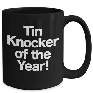 May include: Black ceramic coffee mug with white text that reads "Tin Knocker of the Year!"