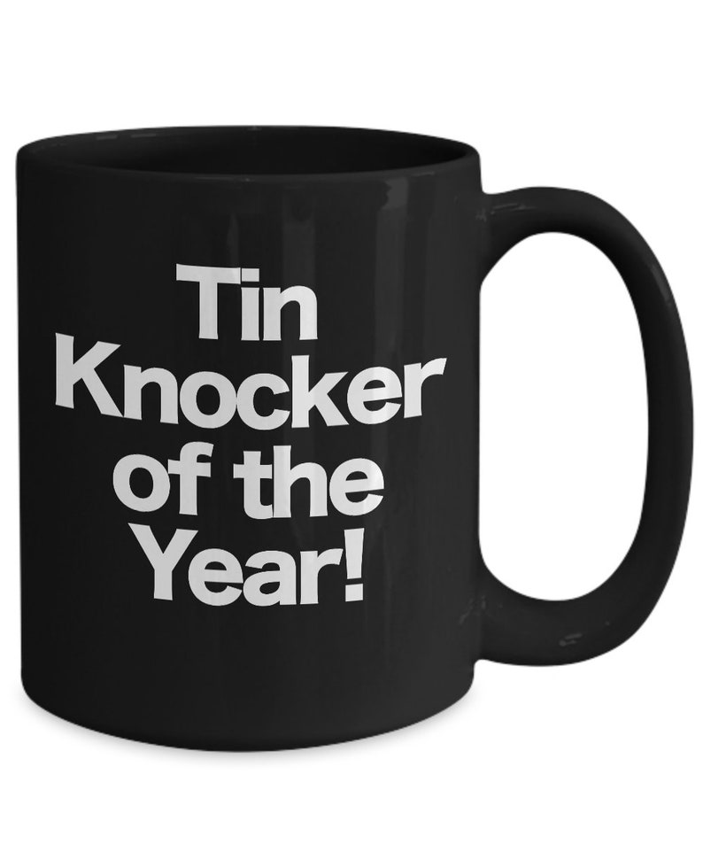 May include: Black ceramic coffee mug with white text that reads "Tin Knocker of the Year!"