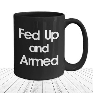 May include: Black ceramic coffee mug with white text that reads "Fed Up and Armed".
