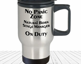 May include: A silver travel mug with a black lid and handle. The mug has the text "No Panic Zone Natural Born Stage Manager On Duty" printed on it.