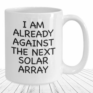 May include: White ceramic coffee mug with black text that reads "I am already against the next solar array".