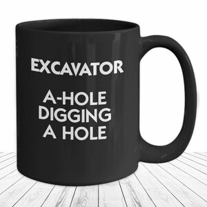 May include: Black coffee mug with white text that reads "Excavator A-hole digging a hole".