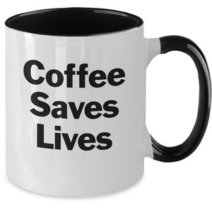 May include: White coffee mug with a black rim and handle. The mug has black text that reads "Coffee Saves Lives."