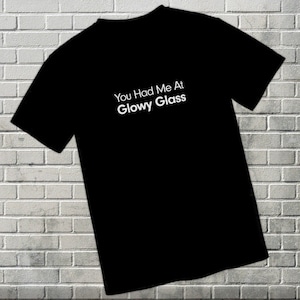 May include: Black t-shirt with white text that reads "You Had Me At Glowy Glass".