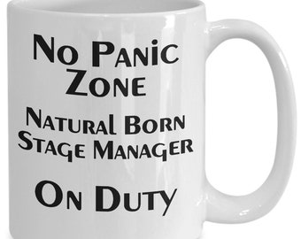 May include: White ceramic coffee mug with black text that reads "No Panic Zone Natural Born Stage Manager On Duty".