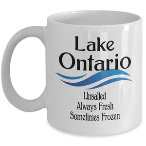 May include: White ceramic coffee mug with a black and blue design. The mug says "Lake Ontario" with a blue wave design and the text "Unsalted Always Fresh Sometimes Frozen".