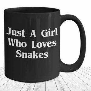 Könnte beinhalten: Schwarze Kaffeetasse mit weißem Text, der "Just A Girl Who Loves Snakes" lautet.