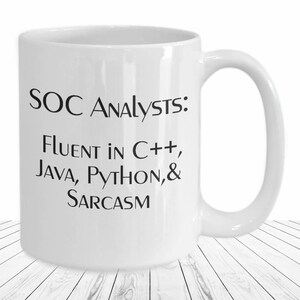 May include: White ceramic mug with black text that reads "SOC Analysts: Fluent in C++, Java, Python, & Sarcasm".