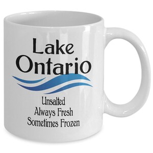May include: White ceramic coffee mug with a blue and white wave design and the text "Lake Ontario Unsalted Always Fresh Sometimes Frozen".