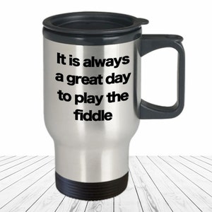 May include: Stainless steel travel mug with a black lid and handle. The mug has the text "It is always a great day to play the fiddle" printed on it.