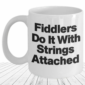 May include: White ceramic coffee mug with black text that reads "Fiddlers Do It With Strings Attached".