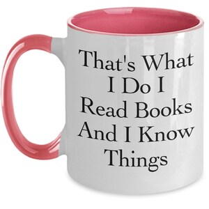 May include: White coffee mug with a pink rim and handle. The mug has black text that reads "That's What I Do I Read Books And I Know Things."