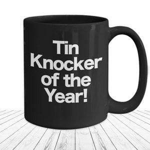 Black Ceramic Coffee Cup 15 fl oz Mug with bold white font in the center that says "Tin Knocker of the Year"
