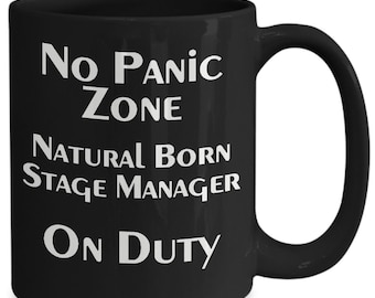 May include: Black coffee mug with white text that reads "No Panic Zone Natural Born Stage Manager On Duty".