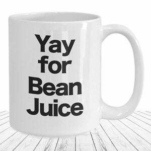 May include: White ceramic coffee mug with black text that reads "Yay for Bean Juice".