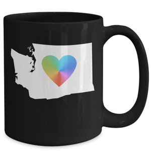 May include: Black coffee mug featuring a white outline of the state of Washington with a rainbow heart in the centre.