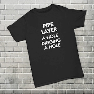 May include: Black t-shirt with white text that reads "PIPE LAYER A-HOLE DIGGING A HOLE"