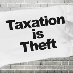 May include: A white piece of paper with the text "Taxation is Theft" printed in black letters. The paper is crumpled and partially torn, and it is attached to a brick wall.
