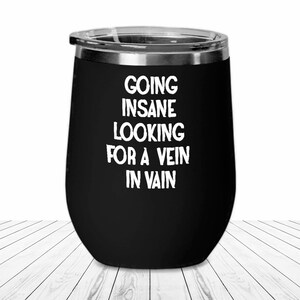 May include: Black stainless steel wine tumbler with white text that reads "Going Insane Looking For A Vein In Vain".