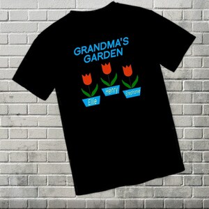 May include: Black t-shirt with the text "Grandma's Garden" in blue and white. Three red tulips with green stems are in blue pots with the names "Ellie", "Henry", and "Stephanie" written below.