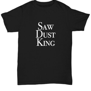 Peut inclure: T-shirt noir avec du texte blanc qui dit "SAW DUST KING".