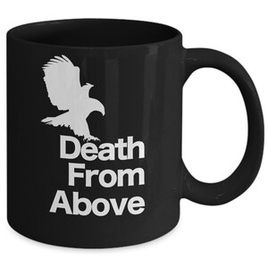 以下が含まれることがあります： 白い鷲のシルエットと「Death From Above」という文字が書かれた黒いセラミック製のコーヒーカップです。