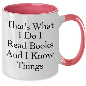 May include: White ceramic coffee mug with a pink rim and handle. The mug has black text that reads "That's What I Do I Read Books And I Know Things."