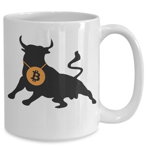 Könnte beinhalten: Weiße Keramiktasse mit einer schwarzen Silhouette eines Bullen mit einem goldenen Bitcoin-Symbol um den Hals.