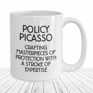 May include: White ceramic coffee mug with black text that reads "Policy Picasso Crafting Masterpieces of Protection with a Stroke of Expertise".
