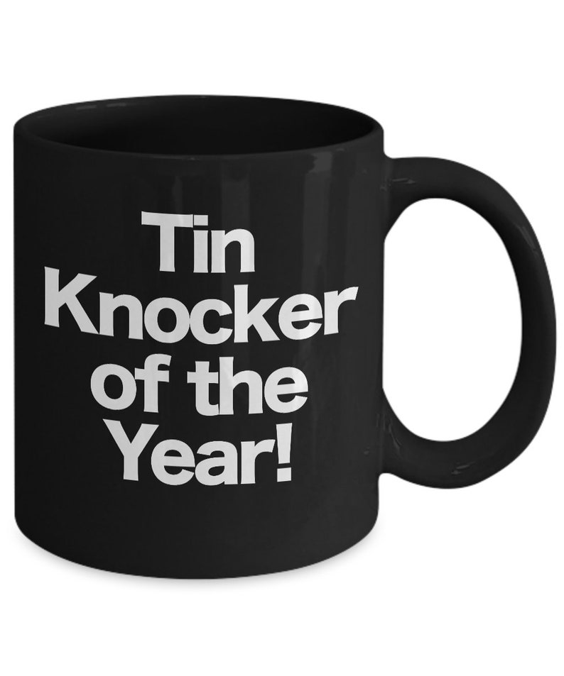 May include: Black ceramic coffee mug with white text that reads "Tin Knocker of the Year!"