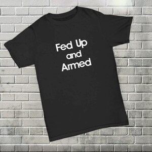 Könnte beinhalten: Schwarzes T-Shirt mit weißem Text, der "Fed Up and Armed" lautet.
