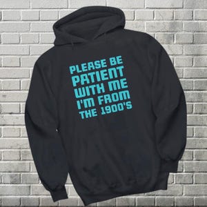 May include: Black hooded sweatshirt with the text "Please be patient with me I'm from the 1900's" in teal blue.
