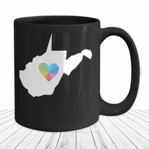 Könnte beinhalten: Schwarze Kaffeetasse mit einer weißen Umrandung des Bundesstaates West Virginia und einem Regenbogenherz in der Mitte.