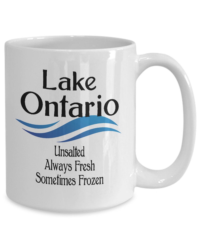 May include: White ceramic coffee mug with a black and blue design. The mug features the text "Lake Ontario" with a blue wave design and the text "Unsalted Always Fresh Sometimes Frozen".