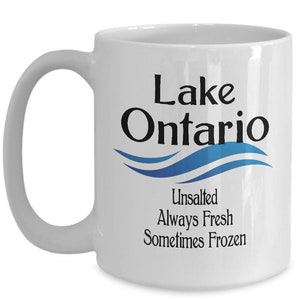 May include: White ceramic coffee mug with a black and blue design. The mug features the text "Lake Ontario" with a blue wave design and the text "Unsalted Always Fresh Sometimes Frozen".