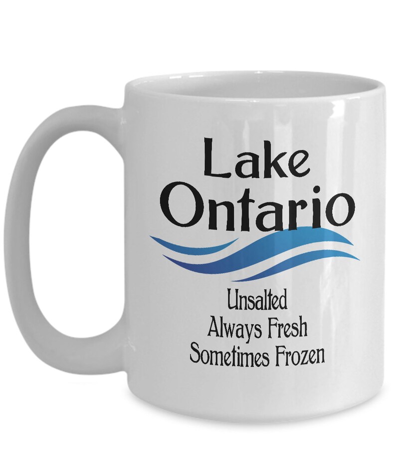 May include: White ceramic coffee mug with a black and blue design. The mug features the text "Lake Ontario" with a blue wave design and the text "Unsalted Always Fresh Sometimes Frozen".